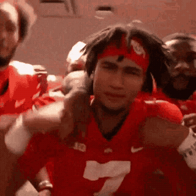 A Man Wearing A Red Jersey And A Headband Is Standing In Front Of A Group Of People . GIF