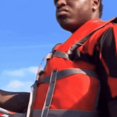 A Man Wearing A Red Life Jacket Is Holding A Steering Wheel GIF