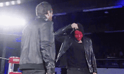 A Man Wearing A Red Mask Stands Next To Another Man In A Black Jacket GIF