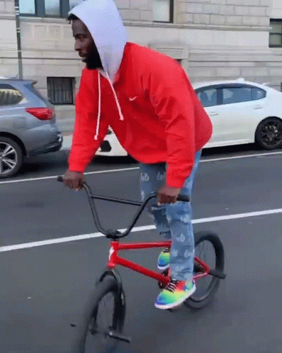 A Man Wearing A Red Nike Jacket Is Riding A Red Bike GIF