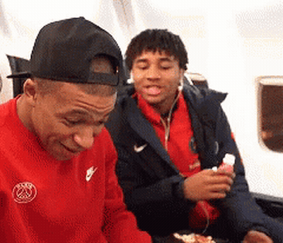 A Man Wearing A Red Nike Shirt Is Sitting Next To Another Man Wearing A Black Hat . GIF