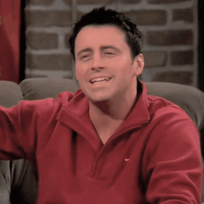 A Man Wearing A Red Nike Sweater Smiles While Sitting On A Couch GIF