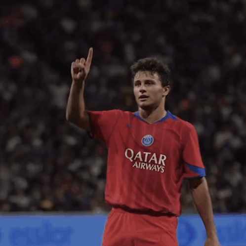 A Man Wearing A Red Qatar Airways Jersey Holds Up His Hand GIF