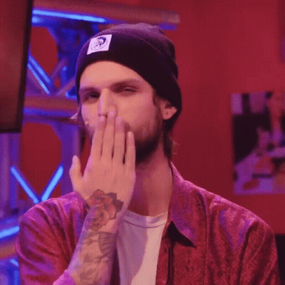 A Man Wearing A Red Shirt And A Black Beanie Is Covering His Mouth GIF