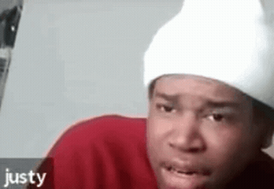 A Man Wearing A Red Shirt And A White Beanie Is Making A Funny Face . GIF