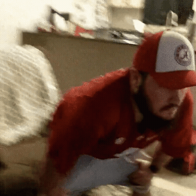 A Man Wearing A Red Shirt And A White Hat With A Logo On It Is Kneeling Down GIF