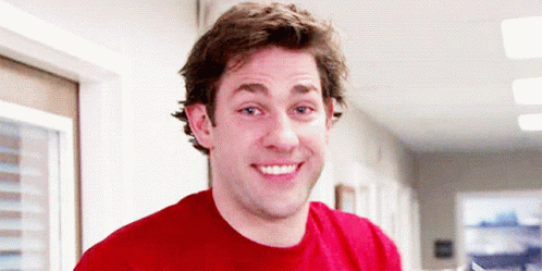 A Man Wearing A Red Shirt Is Smiling In A Hallway GIF