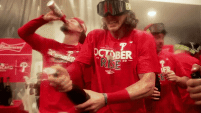 A Man Wearing A Red Shirt That Says October Rise Is Drinking A Beer GIF
