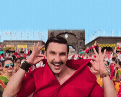A Man Wearing A Red Shirt With A Mustache Is Smiling In Front Of A Crowd GIF