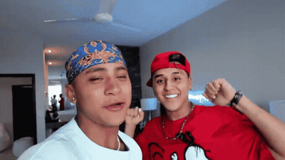 A Man Wearing A Red Shirt With Mickey Mouse On It Stands Next To Another Man Wearing A Bandana GIF