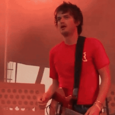 A Man Wearing A Red Shirt With The Letter B On It Is Playing A Guitar GIF