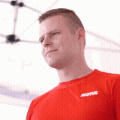 A Man Wearing A Red Shirt With The Word Motul On It Is Standing In Front Of A White Tent . GIF