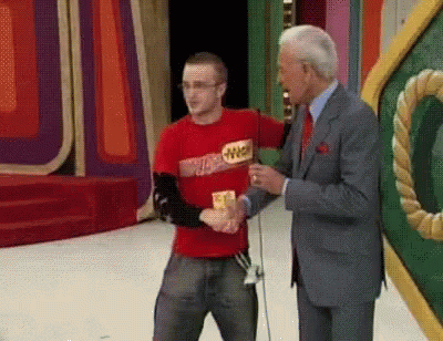 A Man Wearing A Red Shirt With The Word Winner On It Shakes Hands With Another Man In A Suit GIF