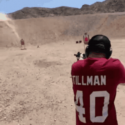 A Man Wearing A Red Shirt With Tillman On The Back Is Shooting A Gun GIF