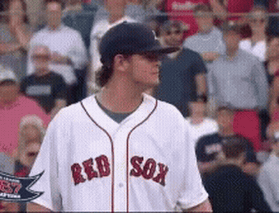 A Man Wearing A Red Sox Jersey Stands In Front Of A Crowd Of People GIF