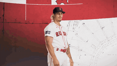A Man Wearing A Red Sox Jersey Stands In Front Of A Red And White Flag GIF
