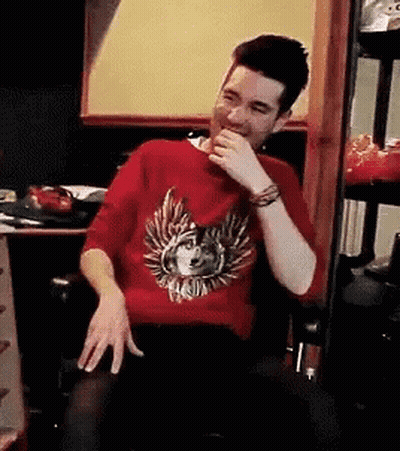 A Man Wearing A Red Sweater With A Wolf On It Is Sitting In A Chair And Laughing . GIF