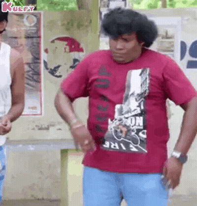 A Man Wearing A Red T-Shirt And Blue Jeans Is Standing In Front Of A Wall . GIF
