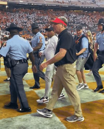 A Man Wearing A Red Visor Is Walking On A Field With Police Officers GIF