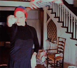 A Man Wearing A Red White And Blue Beanie Is Standing In Front Of A Staircase GIF