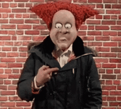 A Man Wearing A Red Wig And A Mask Is Pointing At Something . GIF