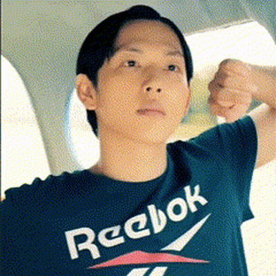A Man Wearing A Reebok T-Shirt Is Flexing His Muscles GIF