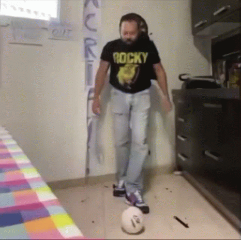 A Man Wearing A Rocky Shirt Is Kicking A Ball GIF
