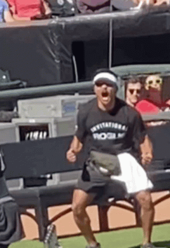 A Man Wearing A Rogue T-Shirt Is Sitting On A Bench On A Baseball Field . GIF