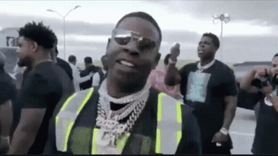 A Man Wearing A Safety Vest And Sunglasses Is Standing In Front Of A Crowd Of People . GIF