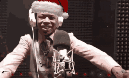 A Man Wearing A Santa Hat And Headphones Is Standing In Front Of A Microphone GIF