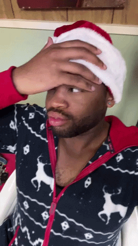 A Man Wearing A Santa Hat Is Covering His Face GIF
