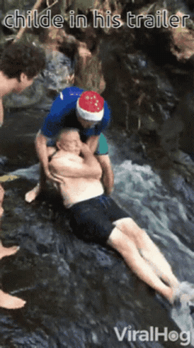 A Man Wearing A Santa Hat Is Helping Another Man In A Waterfall GIF