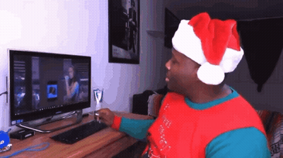 A Man Wearing A Santa Hat Is Sitting In Front Of A Computer Monitor GIF