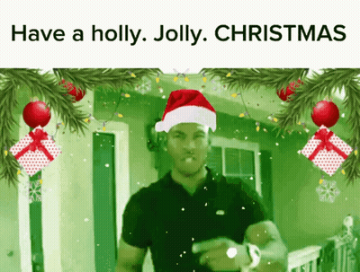 A Man Wearing A Santa Hat Is Surrounded By Christmas Decorations GIF