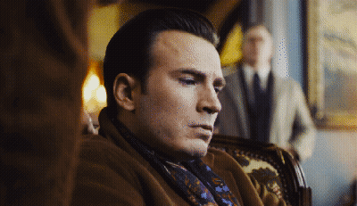 A Man Wearing A Scarf And A Coat Sits In A Chair GIF