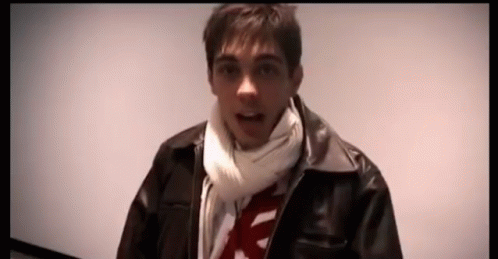 A Man Wearing A Scarf And A Leather Jacket Is Looking At The Camera GIF