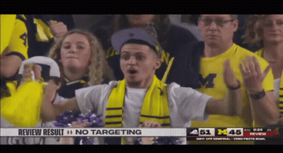 A Man Wearing A Scarf And A Michigan Shirt Stands In The Crowd GIF