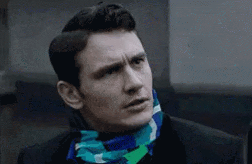 A Man Wearing A Scarf Around His Neck Looks At The Camera GIF