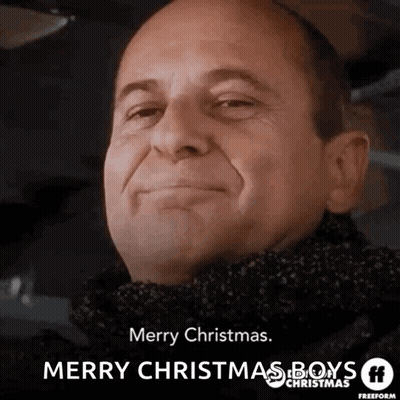 A Man Wearing A Scarf Is Smiling And Wishing Merry Christmas GIF
