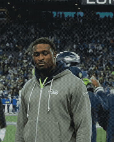 A Man Wearing A Seahawks Hoodie Stands On A Field GIF