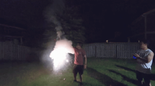 A Man Wearing A Shirt That Says Boo On It Stands In Front Of A Firework Display GIF