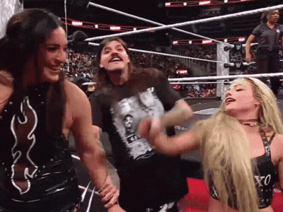 A Man Wearing A Shirt That Says ' G ' On It Is Laughing With Two Women In A Wrestling Ring GIF