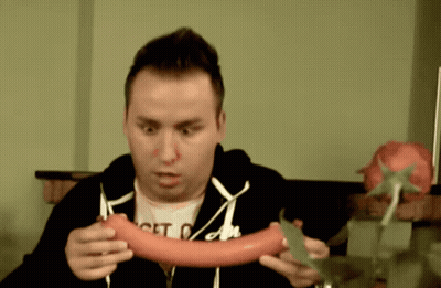 A Man Wearing A Shirt That Says Get On Holds A Sausage GIF