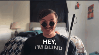 A Man Wearing A Shirt That Says Hey I 'M Blind Is Holding A Cane GIF