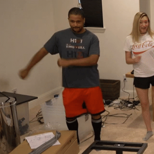 A Man Wearing A Shirt That Says Hit Is Dancing Next To A Woman Wearing A Coca-Cola Shirt GIF