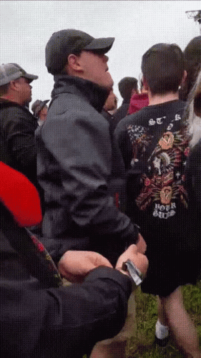 A Man Wearing A Shirt That Says Hot Rod Is Standing In A Crowd Of People GIF