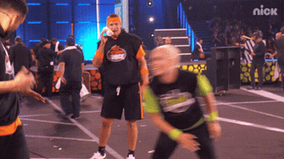 A Man Wearing A Shirt That Says ' Nick ' On It Stands On A Stage GIF
