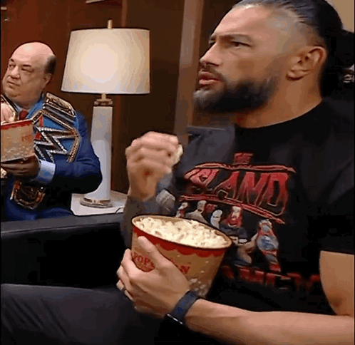 A Man Wearing A Shirt That Says ' Smackdown ' On It Is Eating Popcorn GIF