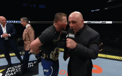 A Man Wearing A Shirt That Says Ultimat Is Being Interviewed By A Man In A Suit GIF