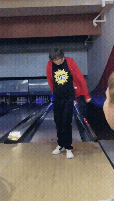 A Man Wearing A Shirt That Says Vs On It Stands On A Bowling Alley GIF